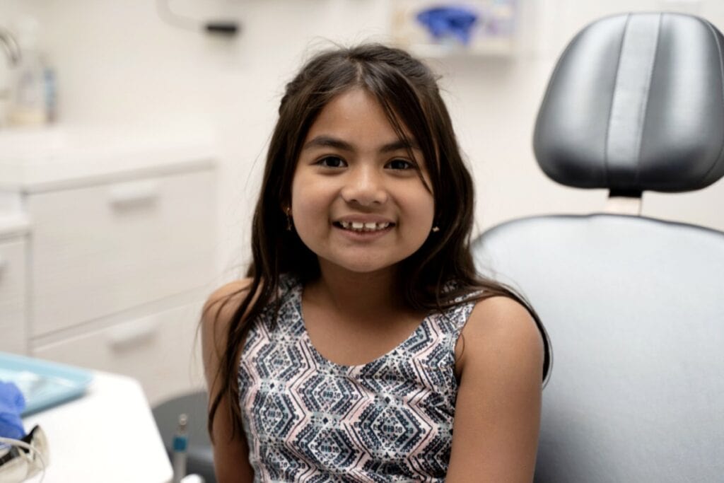 A young girl cautiously sits in a dentist's chair while admiring the various things present in the room.