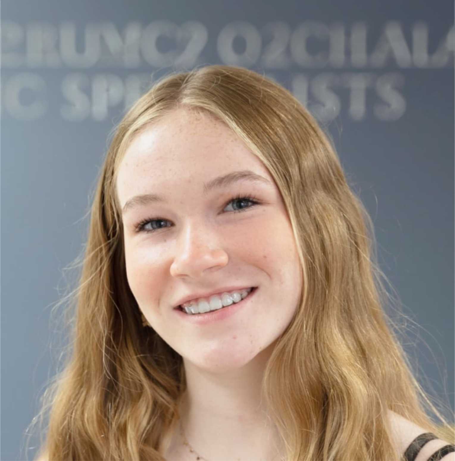 A young woman smiling in front of a sign advertising help.