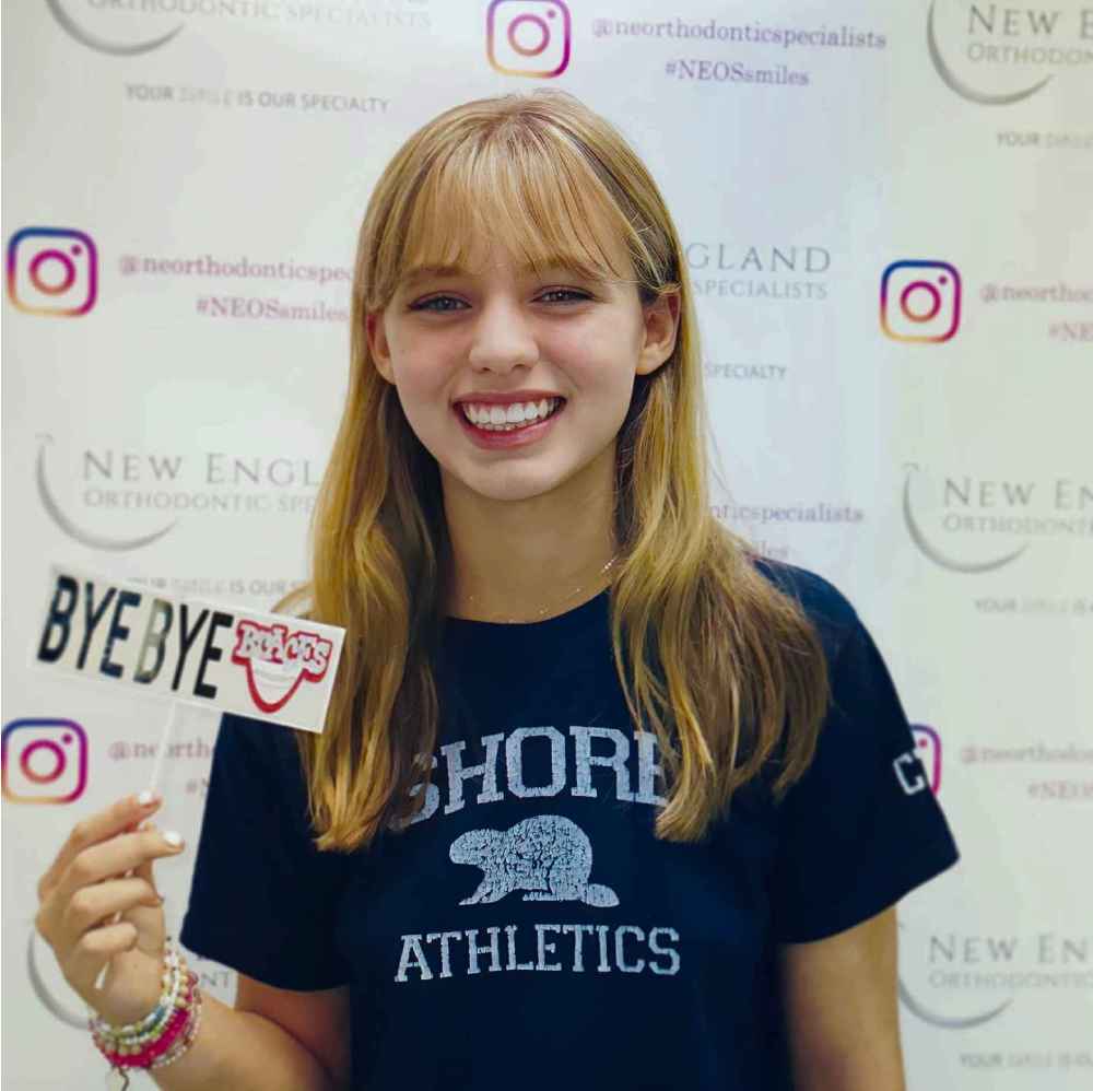 A young girl holding up a sign to help promote New England Orthodontics after braces taken off.