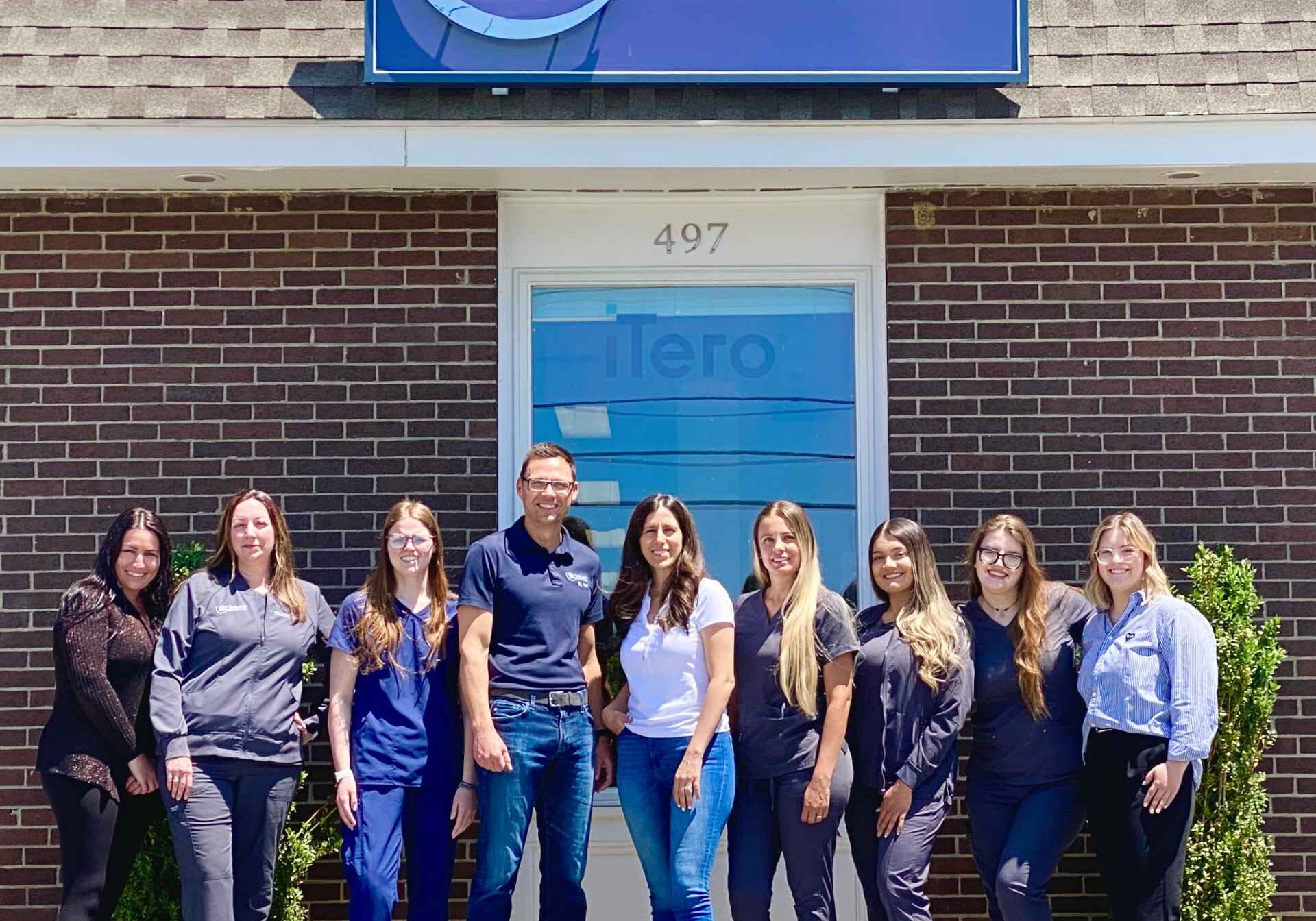 New England orthodontics staff posing in front of their office, inviting YOU to a nice meet.